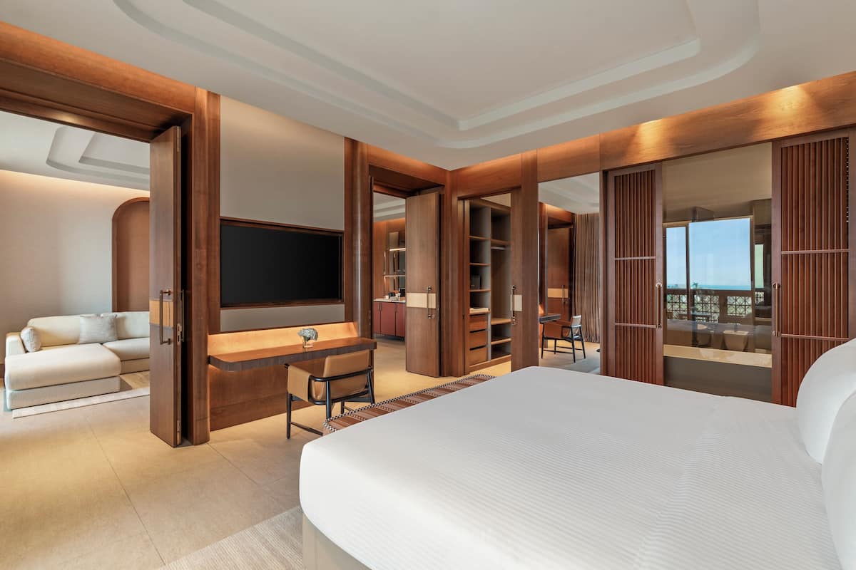 Habitación de hotel moderna con una cama grande, un sofá, un escritorio y un televisor. Tiene un balcón con vistas.