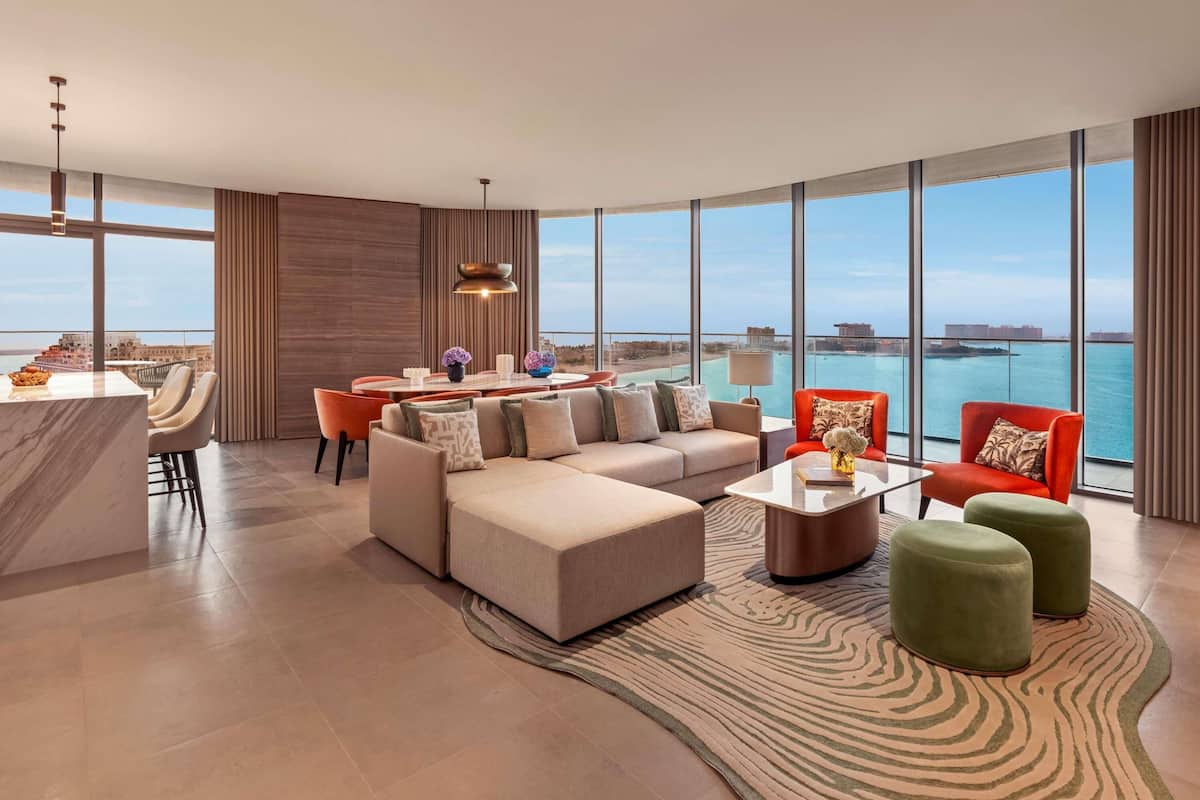 A modern living room with a large window, a sofa, a dining area, and a view of the sea.
