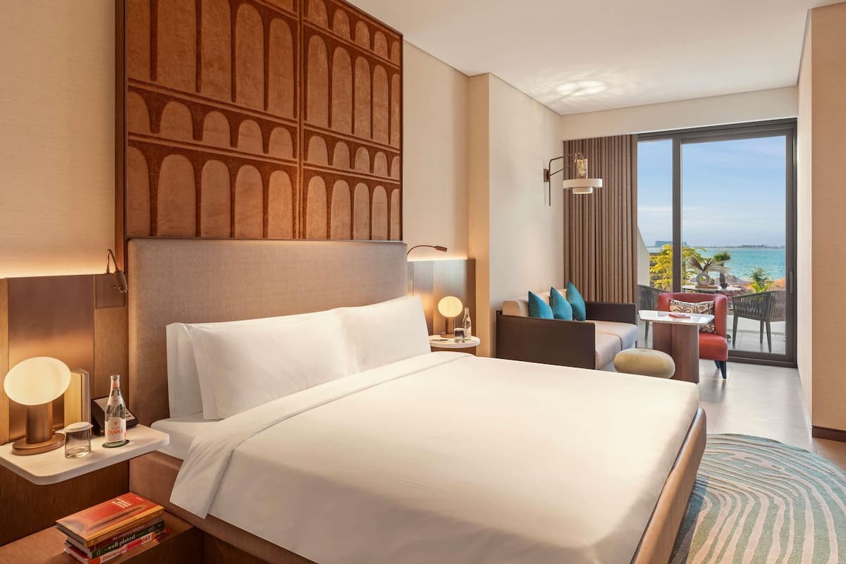 A hotel room with a large bed, a seating area with a view, and a decorative wall panel.