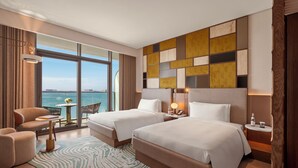 A hotel room with two beds, a sitting area with a view of the sea, and a decorative wall panel. - So/ Ras Al Khaimah Hotel & Resort (Ras Al Khaimah)