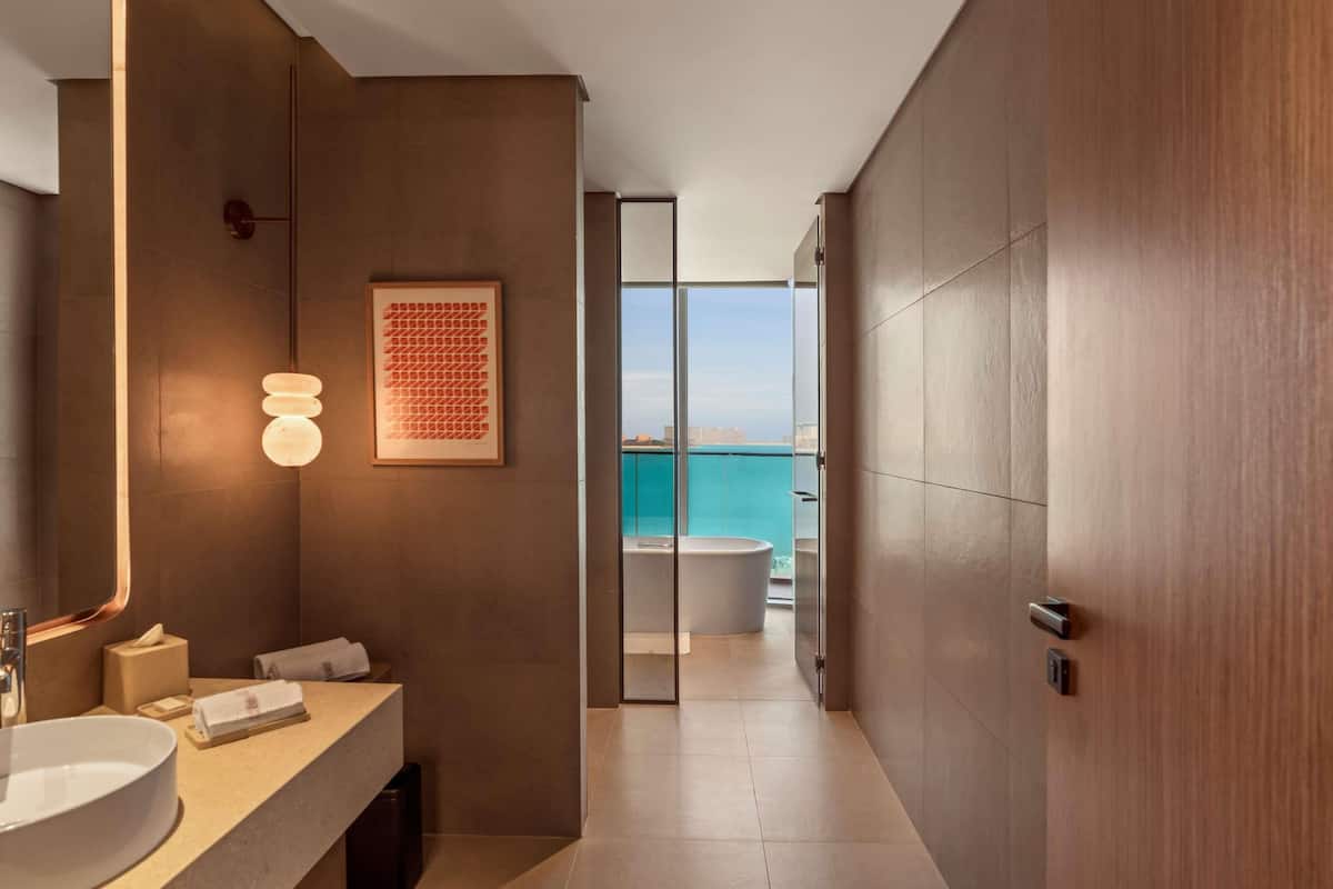 A modern bathroom with a large mirror, a sink, a towel rack, and a framed artwork on the wall.