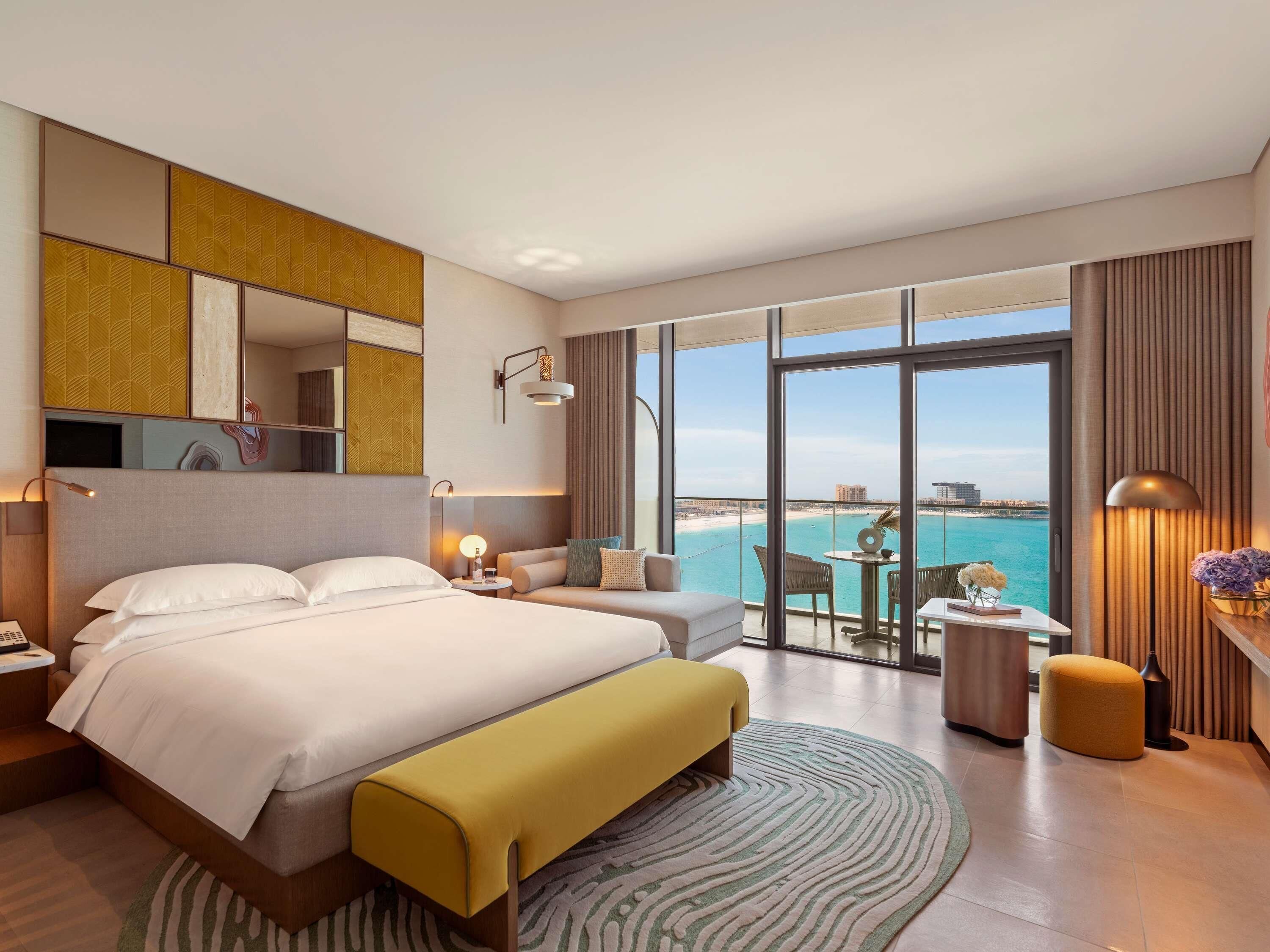 A hotel room with a large bed, a sofa, a small table, and a view of the beach.