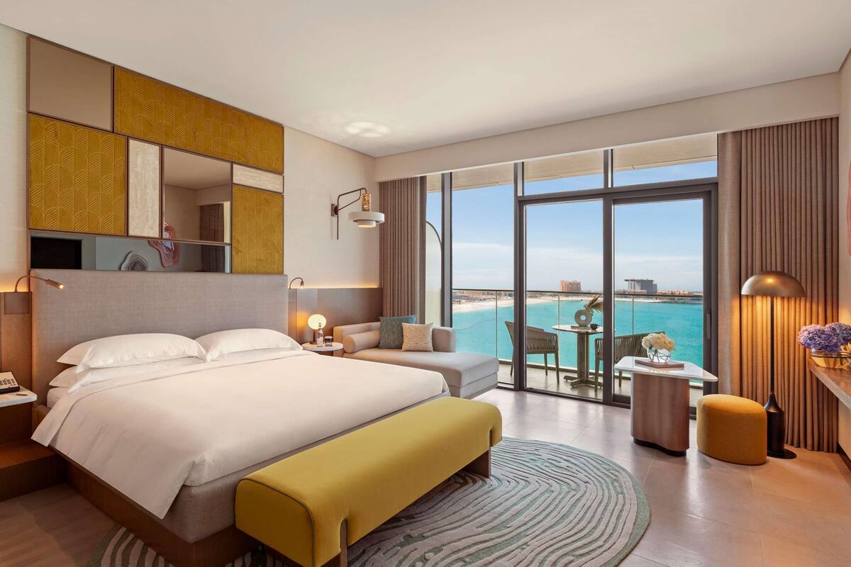 A hotel room with a large bed, a sofa, a small table, and a view of the beach.