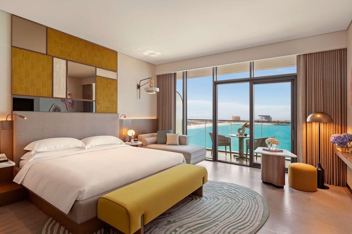 A hotel room with a large bed, a sofa, a small table, and a view of the beach.