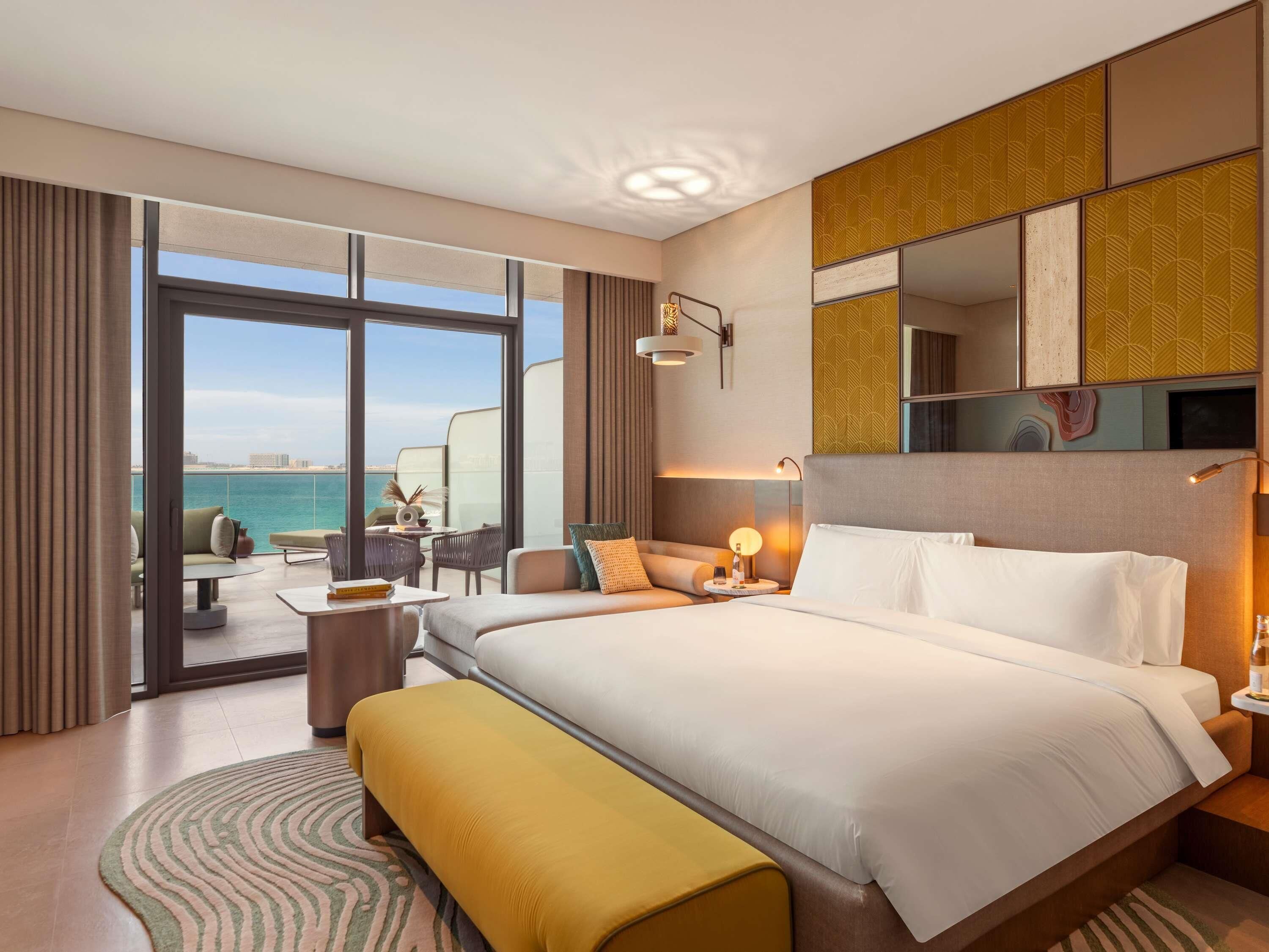 A modern hotel room with a large bed, a seating area with a view of the sea, and a balcony.