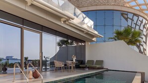 A modern indoor pool with clear blue tiles, a seating area with chairs and a table, and a view of the cityscape through large windows. - So/ Ras Al Khaimah Hotel & Resort (Ras Al Khaimah)