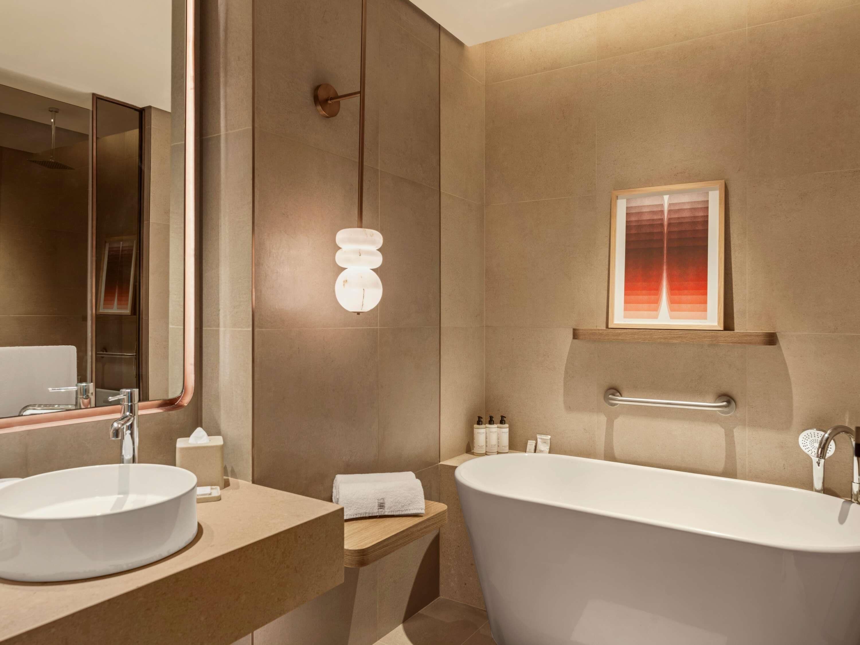 A modern bathroom with a freestanding bathtub, a large mirror, and a framed artwork on the wall.