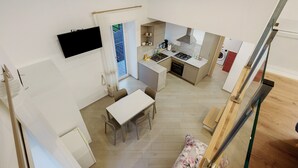 Una cocina moderna con comedor, un televisor montado en la pared y una escalera que lleva a otro nivel.