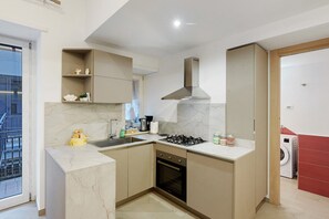 Una cucina compatta con piano cottura a gas, forno e forno a microonde integrato. Si vede una finestra con vista esterna e un'uscita verso una lavanderia.