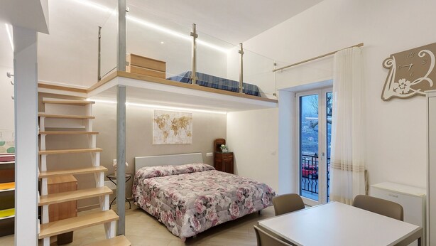 Un dormitorio con cama, escritorio, silla, escalera y ventana con vistas.