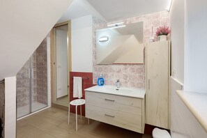 Een badkamer met een douche, wastafel, spiegel en kast.