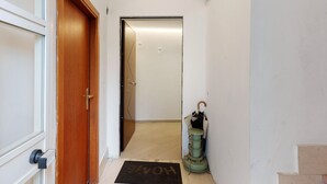 Un pasillo con una puerta de madera, un felpudo y una aspiradora verde.