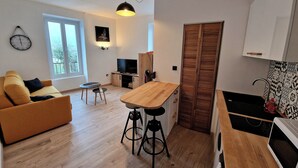 A modern living room with a sofa, a wooden dining table, a TV, and a kitchen area with a microwave. - Nice view apartment - near rue de Siam (Brest)
