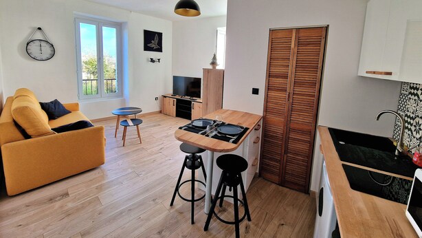A compact living space with a sofa, a dining table with stools, a TV, and a wooden cabinet. - Nice view apartment - near rue de Siam (Brest)
