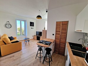 A compact living space with a sofa, a dining table with stools, a TV, and a wooden cabinet. - Apartment with a beautiful view—near Rue de Siam (Brest)