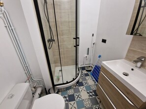 A bathroom with a glass shower enclosure, a white sink with a wooden vanity, and patterned floor tiles. - Apartment with a beautiful view—near Rue de Siam (Brest)