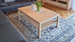 Ein modernes Wohnzimmer mit einer Couch, einem Couchtisch mit einer Vase, einem Fernseher, Lautsprechern und einer Lampe.