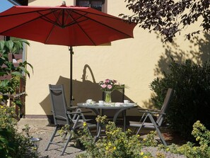 An outdoor patio with a table, chairs, a red umbrella, and a vase of flowers. - Holiday Home 'Ferienhaus Am Leiselbach' with Private Terrace, Private Garden and Wi-Fi (Leisel)