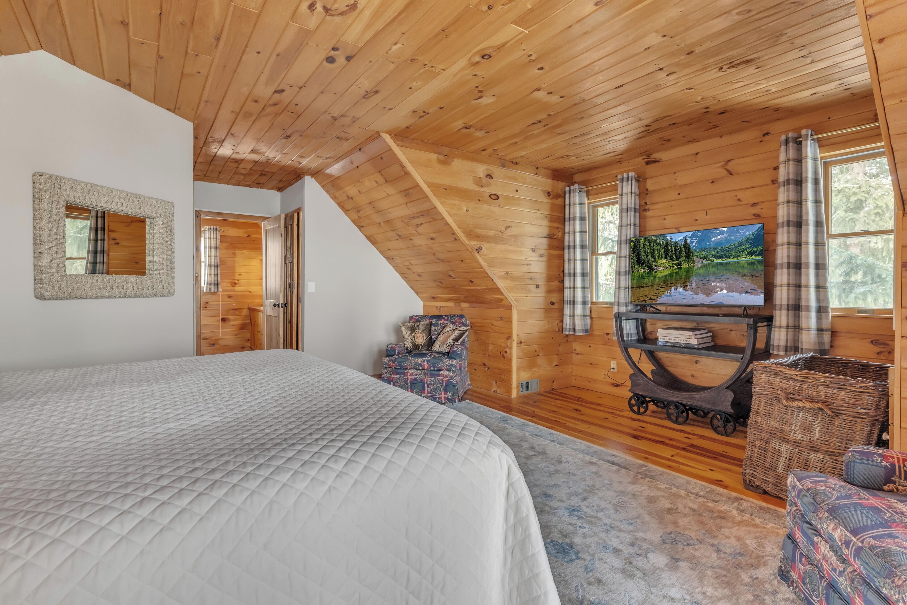 A cozy bedroom with a large bed, wooden ceiling, a TV, and a scenic view.