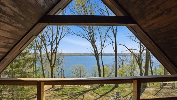 Eine Holzhütte mit einem Dreiecdach, einer Terrasse und Blick auf einen von Bäumen umgebenen See.