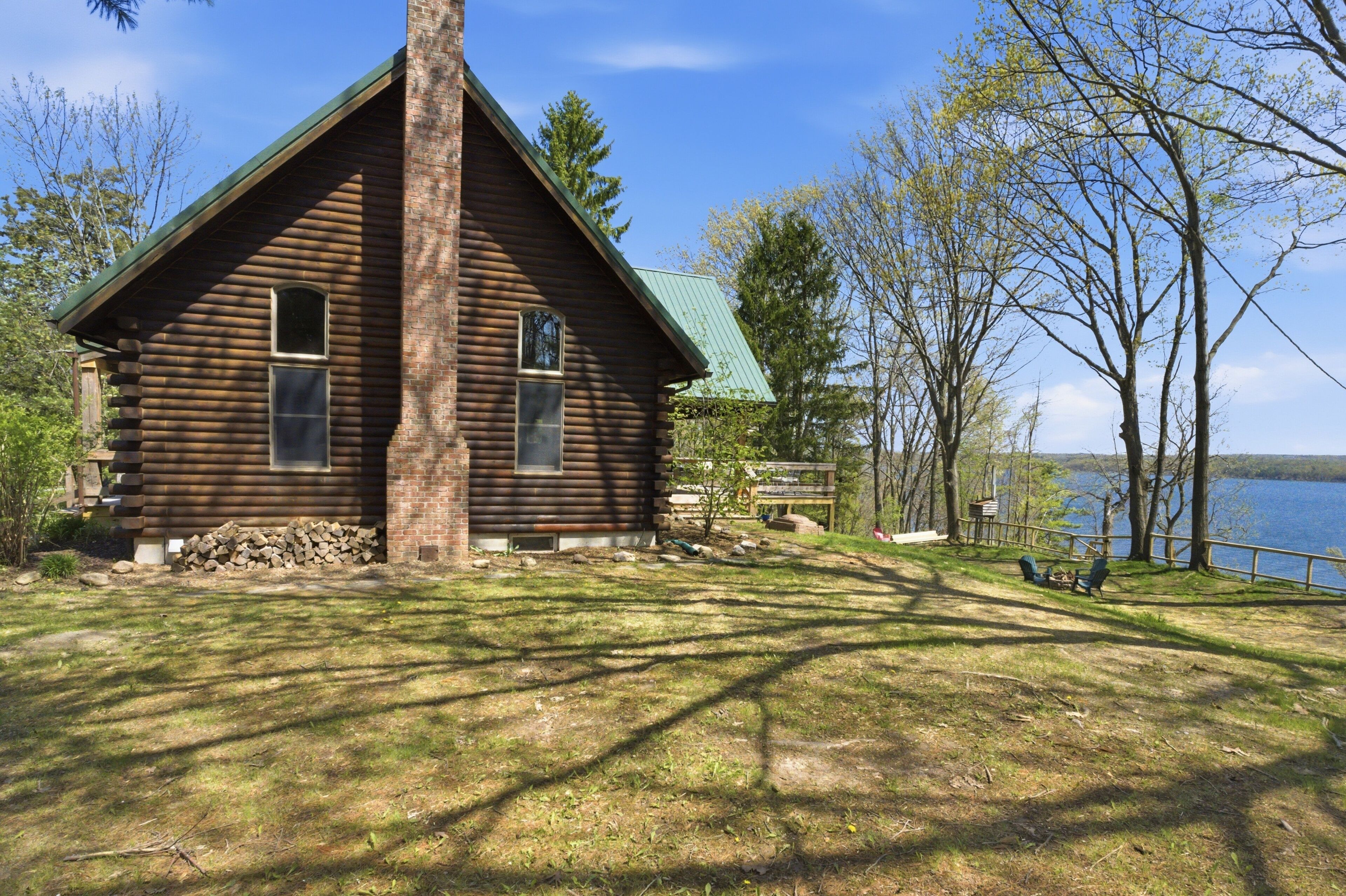A log cabin with a green roof, a stone foundation, and a view of a lake.