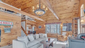 Ein gemütliches Blockhaus-Interieur mit Holzausstattung, einer Couch, einem Couchtisch, einem Kamin und einer Treppe, die zu einer oberen Ebene führt.