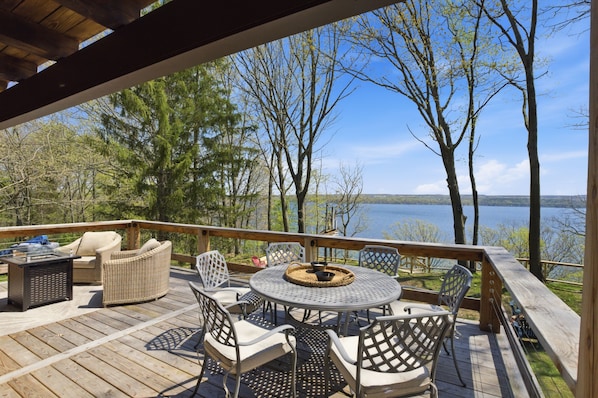 A wooden deck with outdoor furniture, including chairs and a table, overlooking a lake with trees.