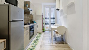A compact kitchen with a refrigerator, stove, microwave, and a dining area with a table and chairs. - Apartment 'Mono' with Wi-Fi and Air Conditioning (La Spezia)
