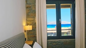 A bedroom with a stone wall, a window with curtains, a bed with white bedding, and a lamp on the nightstand. - Amari stone apartments (Lemnos)