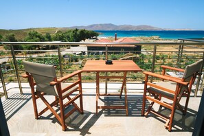 Un balcón con mesa y dos sillas de madera, con vista a un paisaje costero y montañas al fondo.