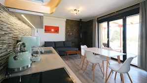 A modern kitchen with a kettle, a coffee maker, and a dining area with a table and chairs. - Amari stone apartments (Lemnos)