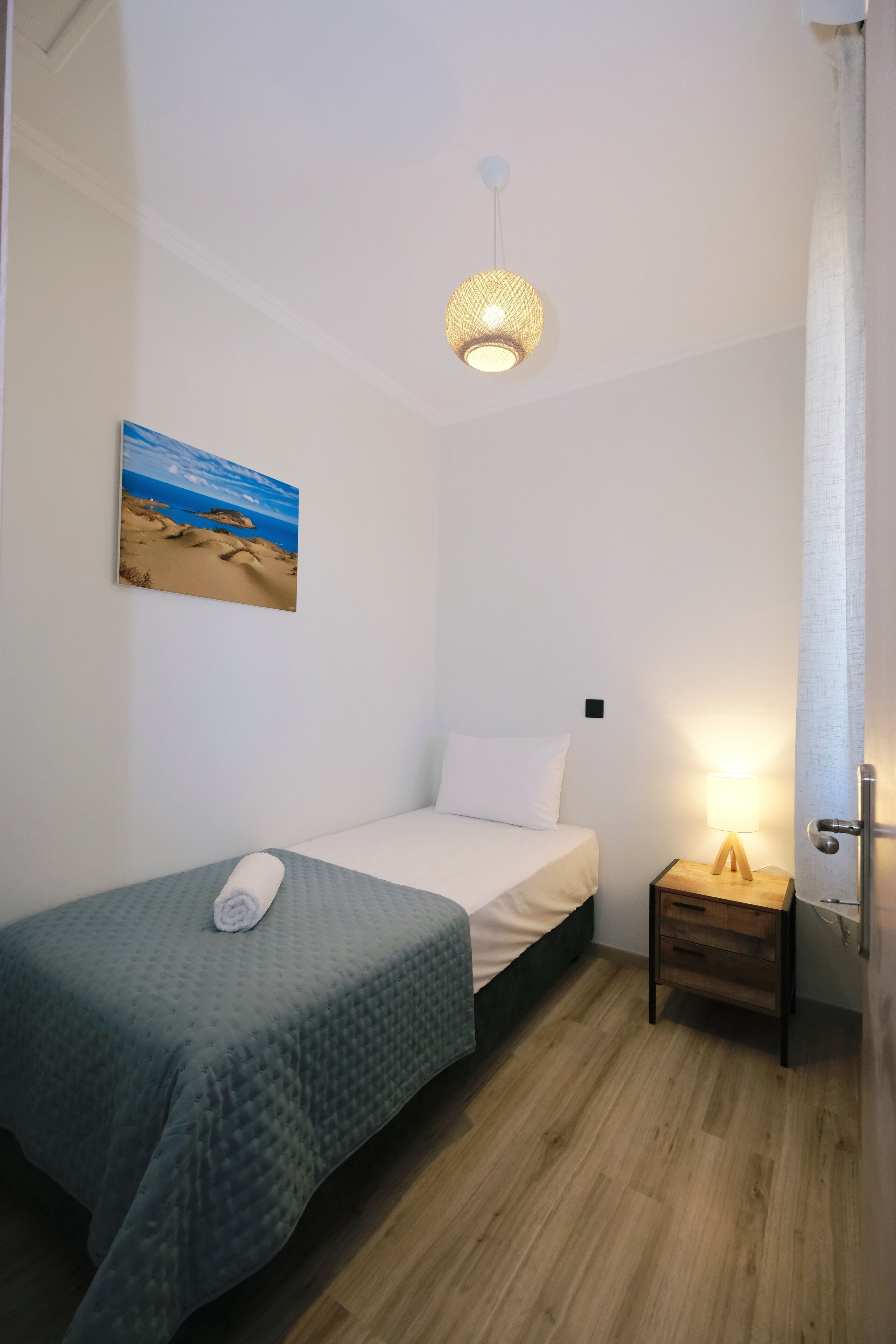 Une petite chambre à coucher, bien rangée, avec un lit simple, une table de chevet avec une lampe, un tableau accroché au mur et un luminaire suspendu au plafond.
