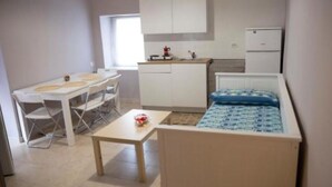 Een kleine, praktische keuken met witte kastjes, een koelkast en een eethoek met een tafel en stoelen.