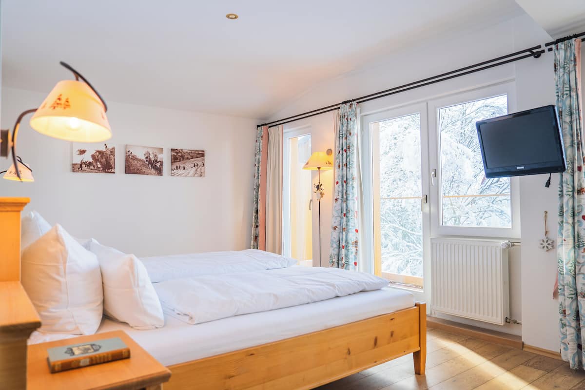 A bedroom with a wooden bed, two bedside lamps, a flat-screen TV, and a window with curtains.