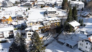A snow-covered residential area with modern houses, including a prominent yellow house and a large building with multiple balconies. - Bergvital Hotel Todtnau (Todtnau)
