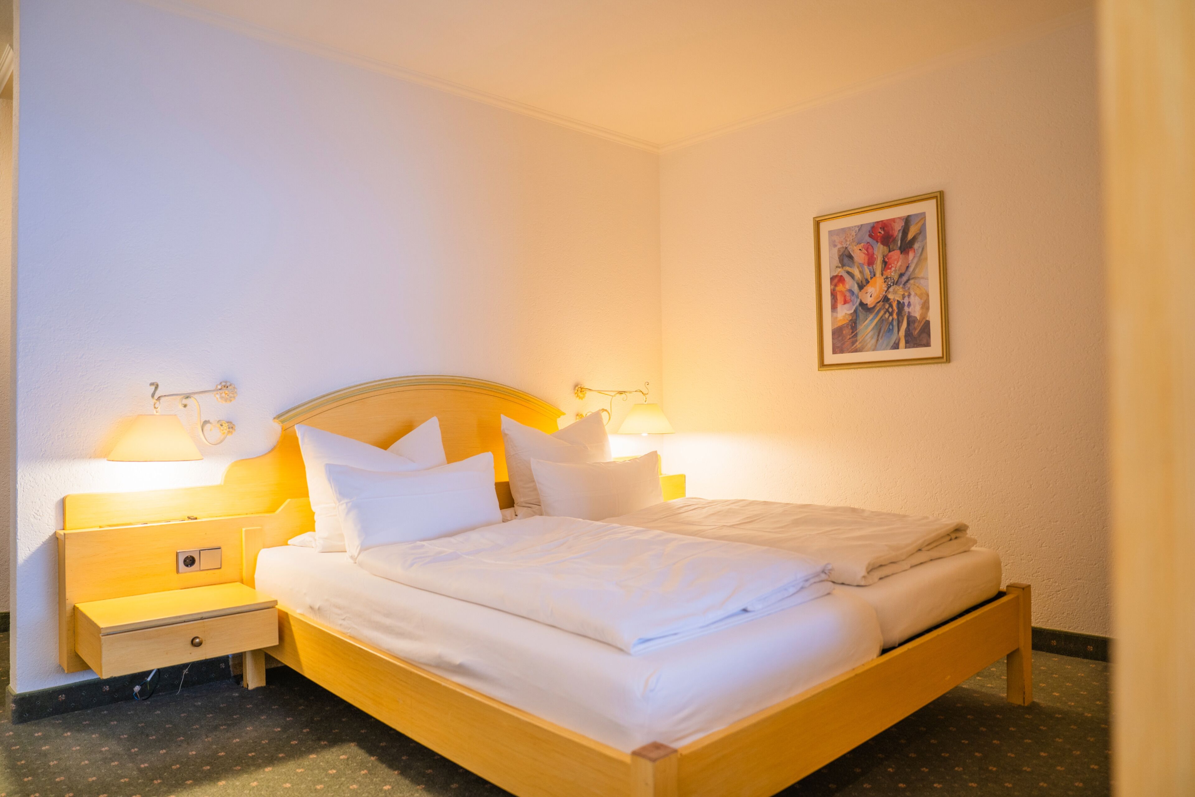 Una cama bien hecha con sábanas blancas, dos mesitas de noche con lámparas y una obra de arte enmarcada en la pared.