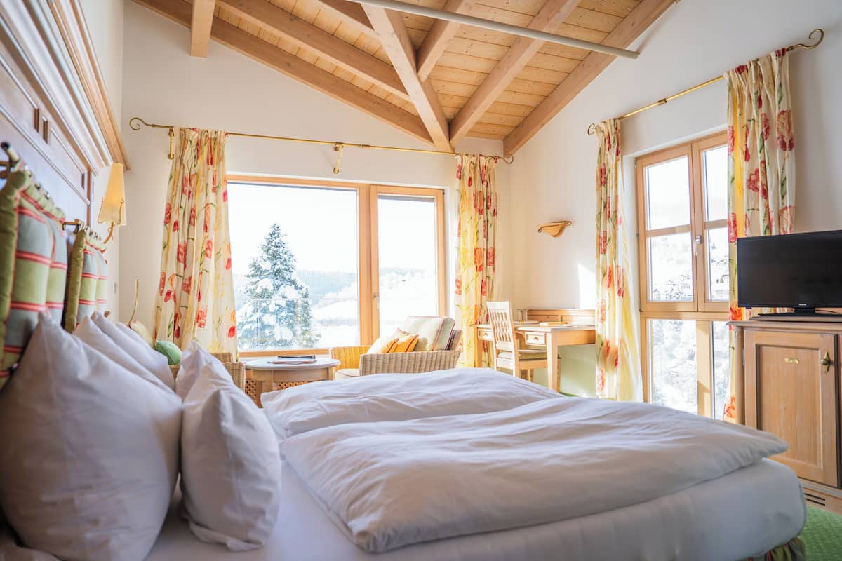 A hotel room with a bed, a television, a desk, and a window with curtains.