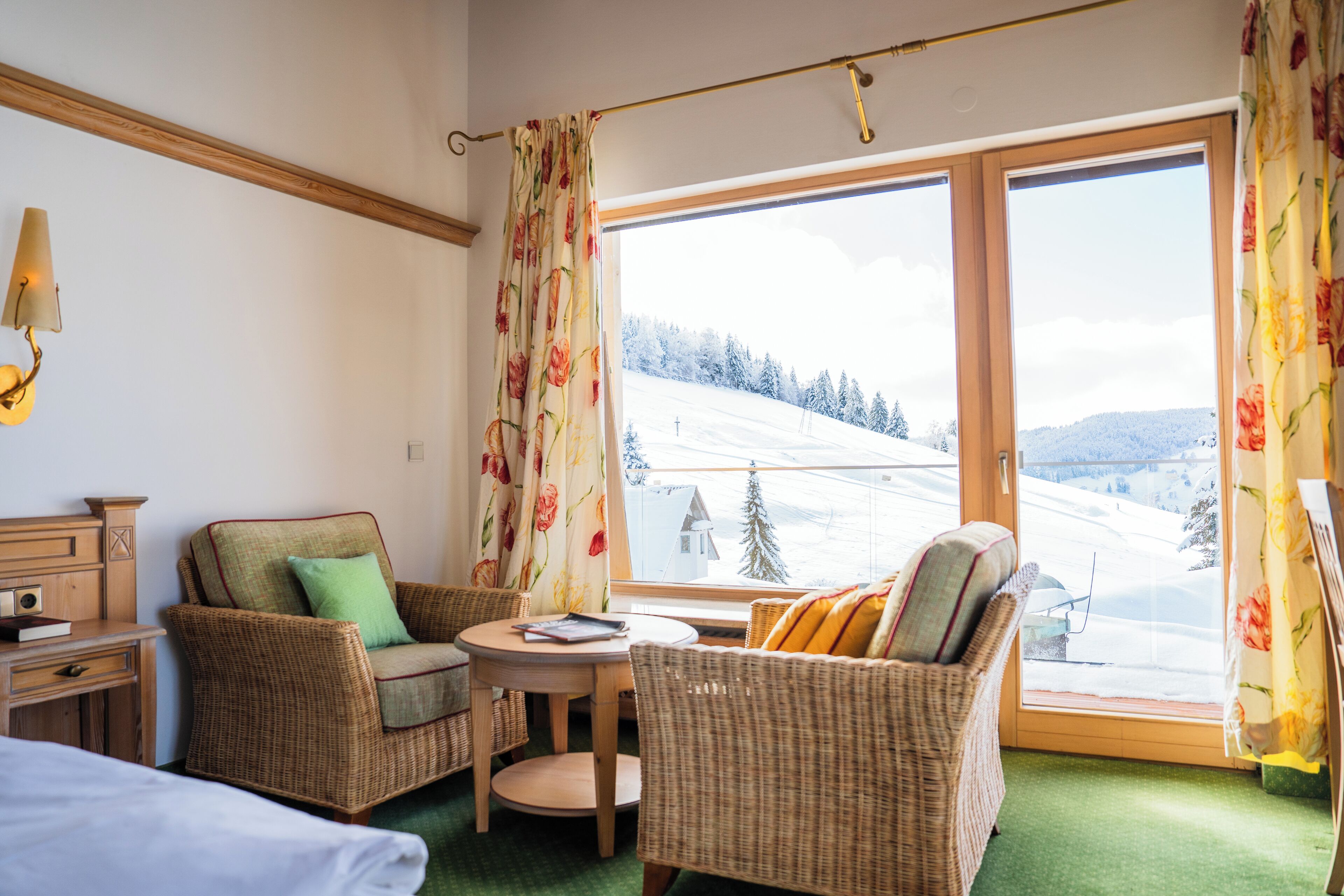 A room with wicker furniture, a small table, and a view of a snowy landscape through large windows.