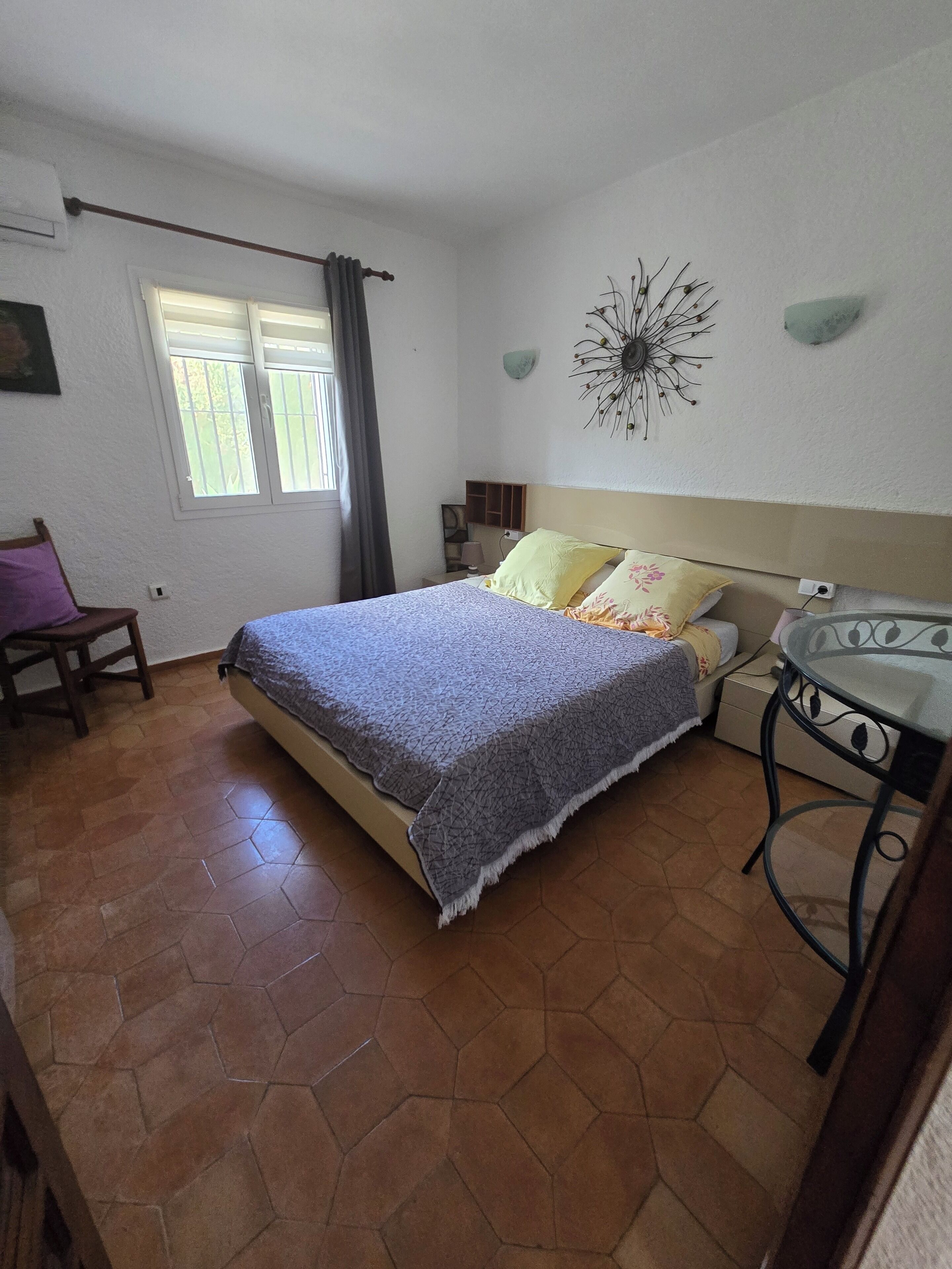 A bedroom with a bed, a chair, a nightstand, a lamp, and a decorative wall piece.