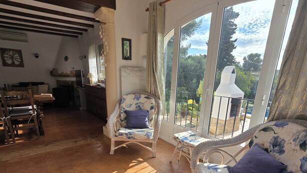 Amplia sala de estar con un ventanal que da a un jardín, amueblada con sillas de mimbre y una mesa de madera.