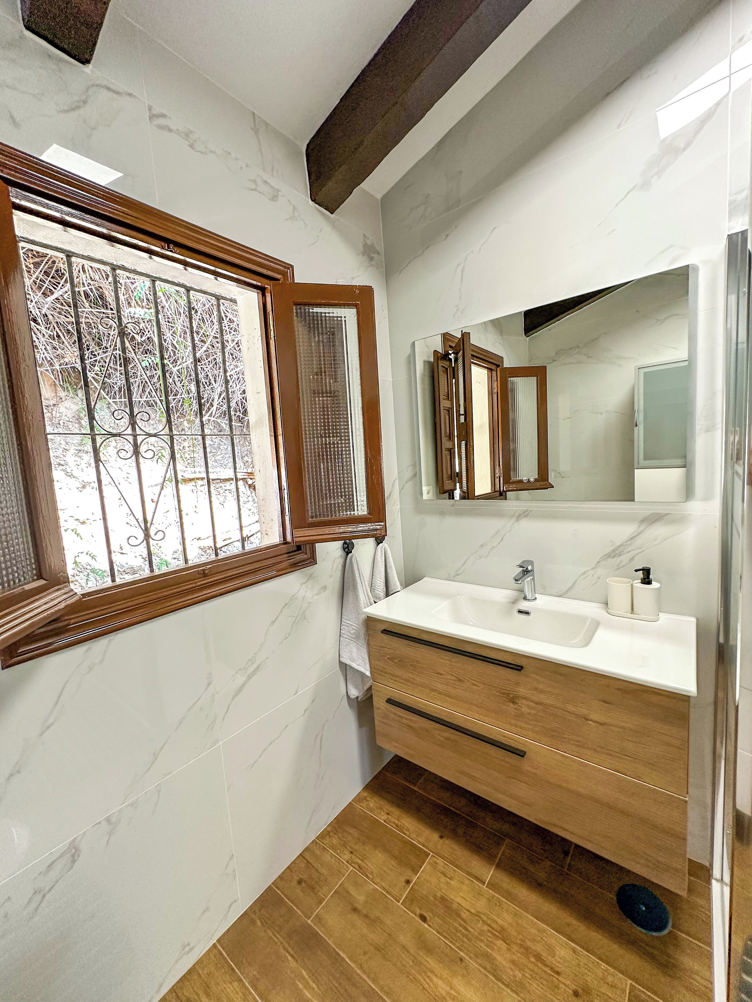 Un baño con pared de mármol, tocador de madera y ventana con barrotes.