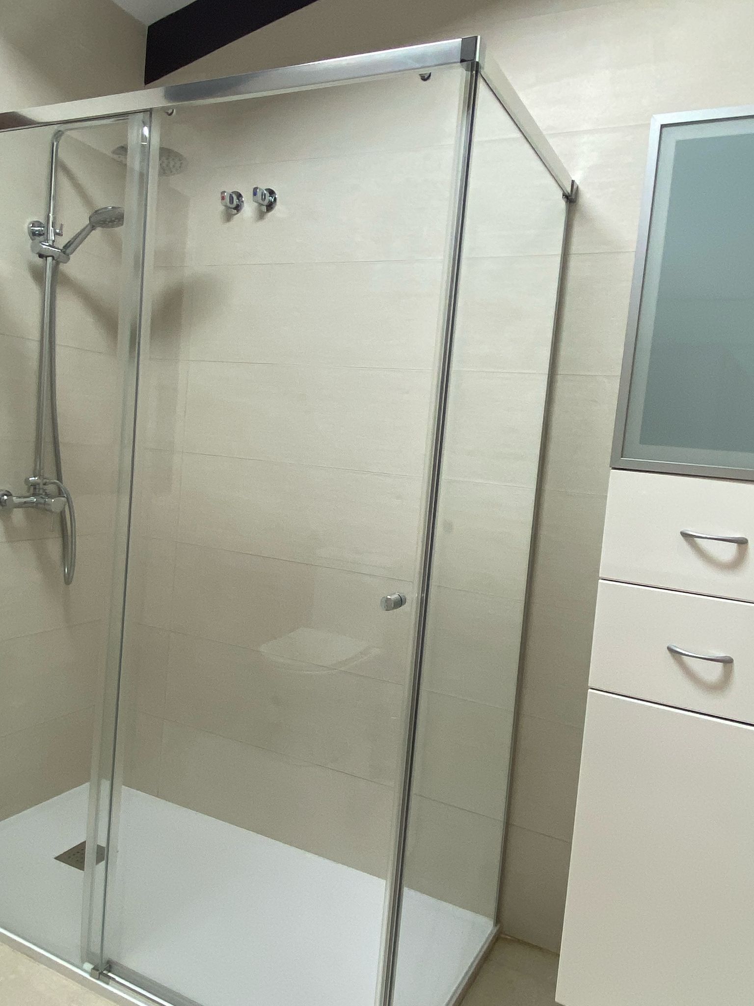 Eine gläserne Dusche mit chromfarbenem Rahmen, einer weißen Fliesenwand und einem weißen Schrank mit Schubladen.