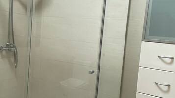 Eine gläserne Dusche mit chromfarbenem Rahmen, einer weißen Fliesenwand und einem weißen Schrank mit Schubladen.