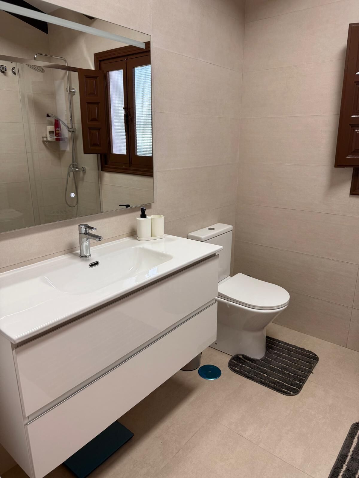 Un baño moderno con lavamanos, espejo y retrete blancos.