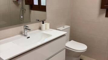 Un baño moderno con lavamanos, espejo y retrete blancos.