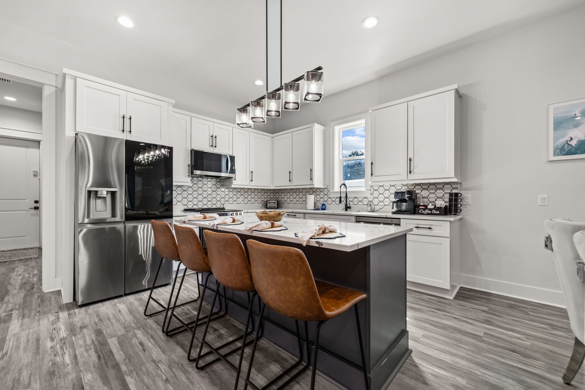 A modern kitchen with stainless steel appliances, a central island with bar stools, and a coffee station.
