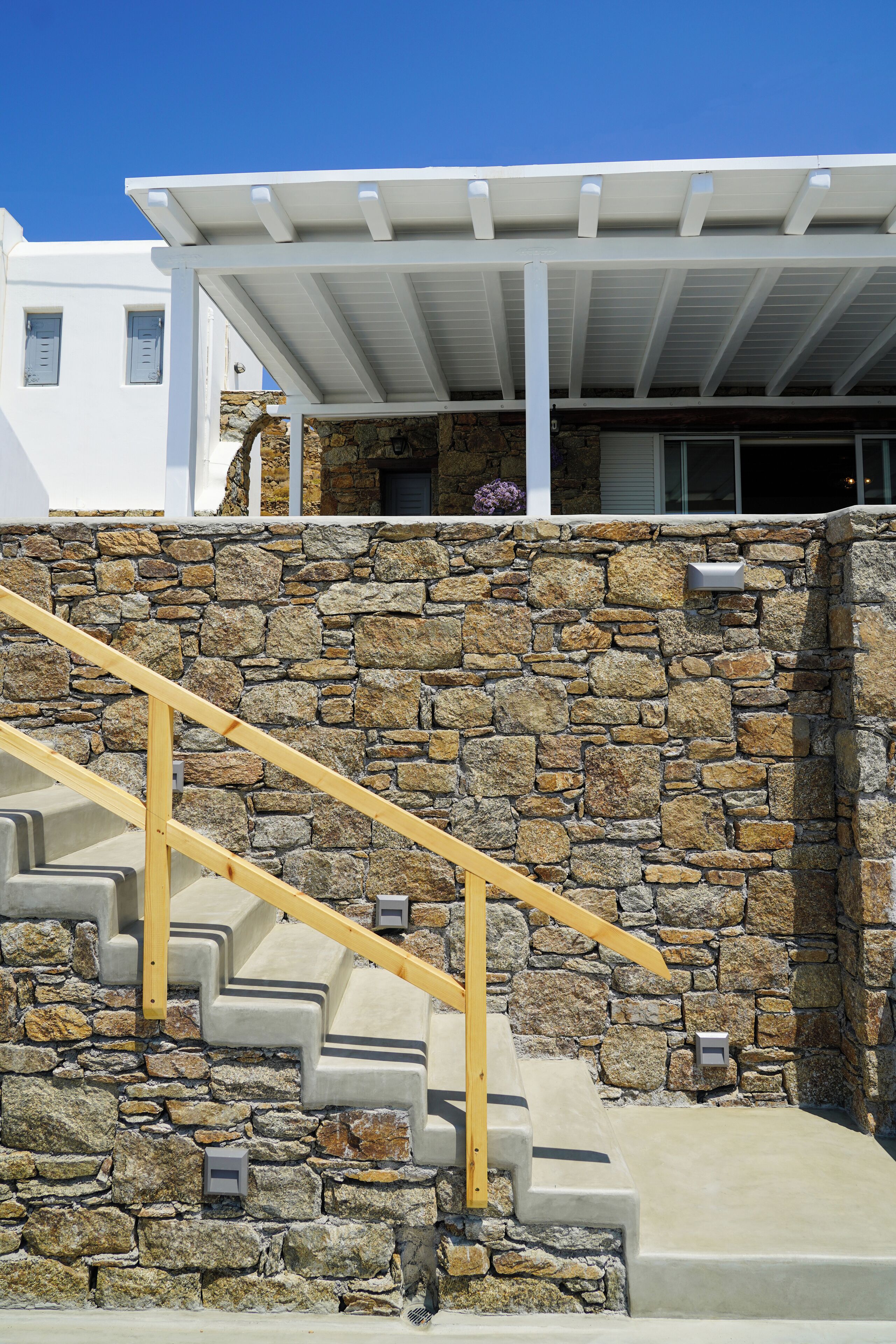 A stone staircase with wooden handrails leading to a white building with a covered porch.