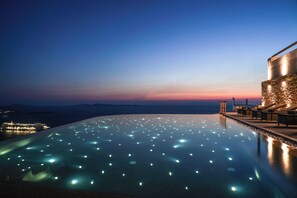 An infinity pool with illuminated lights at dusk, overlooking a coastal landscape with distant city lights. - Aether Mykonos 5BR Port View Villa (Tourlos)
