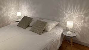 A neatly made bed with white bedding and two patterned pillows, flanked by two bedside tables with lamps. - Aux Pieds des Tours (La Rochelle)