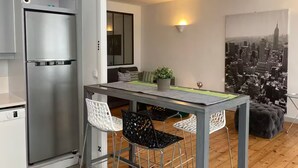 A compact kitchen with a stainless steel refrigerator, a dining area with a table and two chairs, and a cityscape view. - Aux Pieds des Tours (La Rochelle)